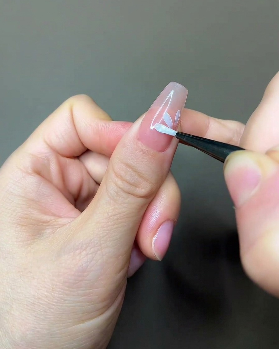 Un pinceau appliquant une couche de top coat mat sur un design floral partiel.