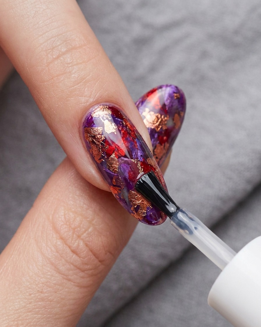 Un pinceau appliquant un top coat brillant transparent sur le nail art en blooming gel rouge et bleu.