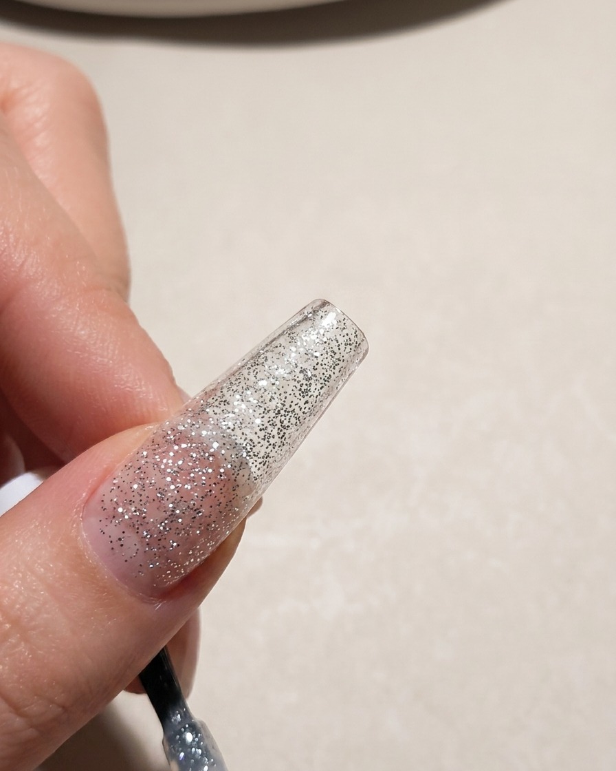 Gros plan sur le bout dun ongle recouvert dun vernis gel à paillettes argentées.