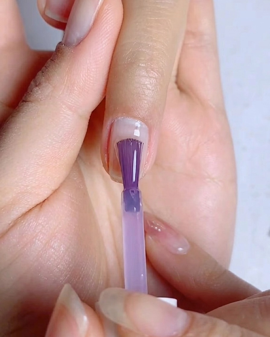 Un pinceau à ongles étalant une fine couche uniforme de vernis gel bleu-violet sur la surface de longle.