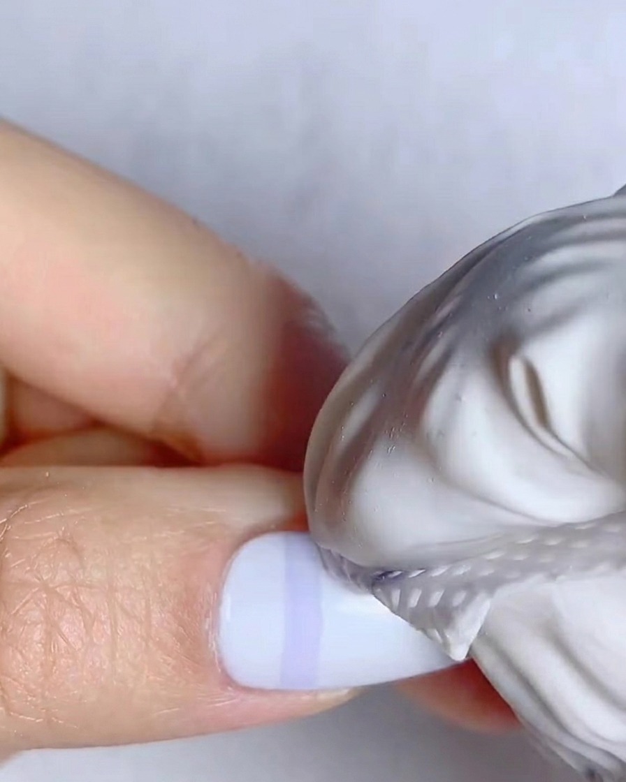 Un pinceau liner fin dessinant des lignes bleues verticales sur un ongle blanc.