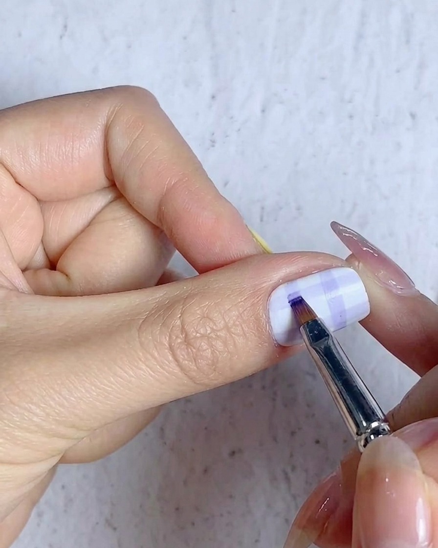 Un pinceau fin remplissant les intersections de la grille sur un design dongle écossais avec du gel bleu.