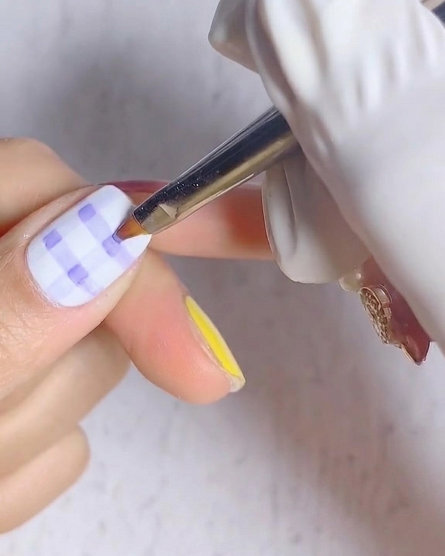 Une vue rapprochée dun ongle avec un motif écossais bleu et blanc placé sous une lampe UV.