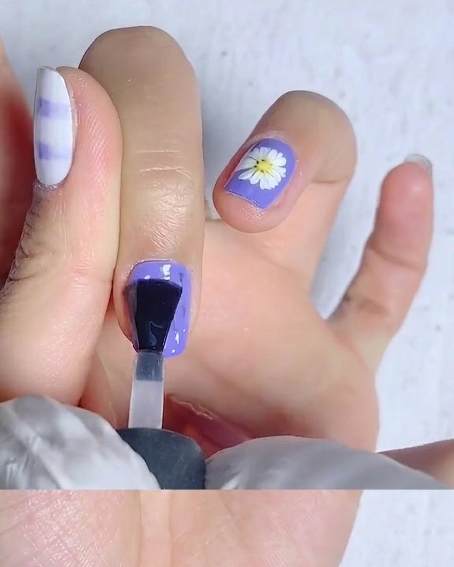 Un pinceau à ongles étalant du top coat mat sur un ongle jaune vif.
