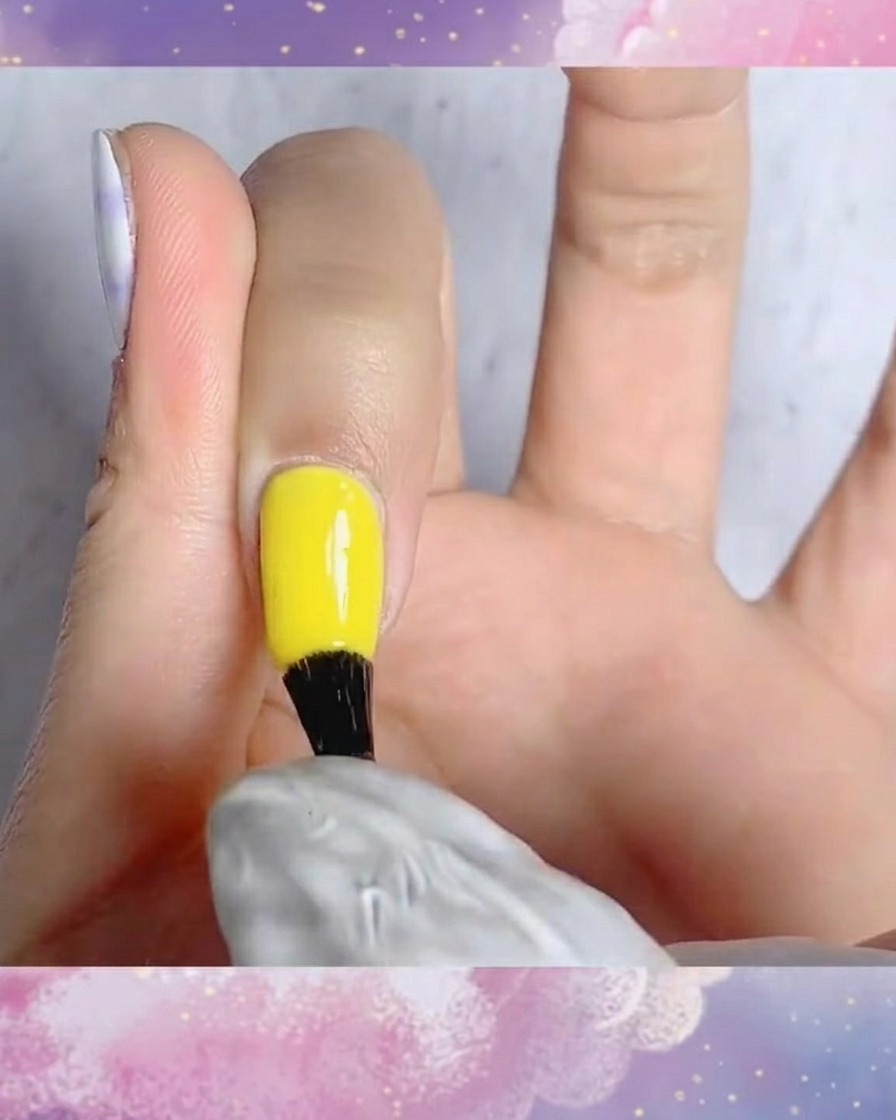 Un pinceau appliquant du top coat mat sur un ongle avec un motif écossais bleu et blanc peint à la main.