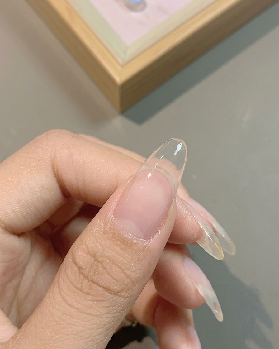 Un pinceau appliquant une base gel blanc lacté translucide sur lensemble de longle naturel.