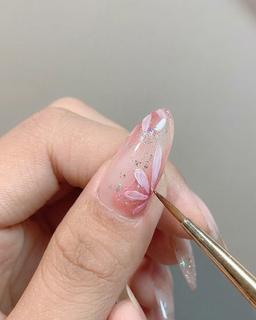 Un pinceau fin déposant une tache concentrée de pigment rose au centre dune marguerite blanche peinte sur un ongle.