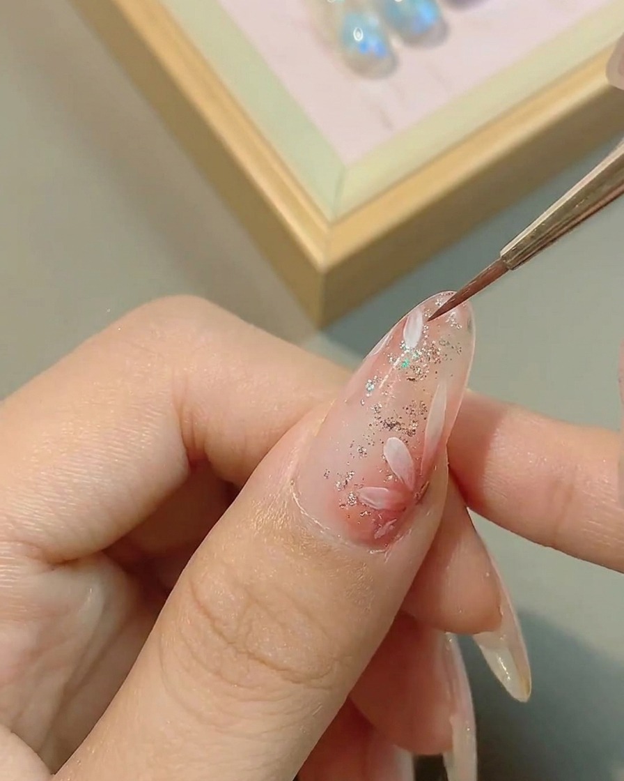 Un pinceau appliquant une couche de finition brillante transparente sur le nail art marguerite terminé, lissant la surface.