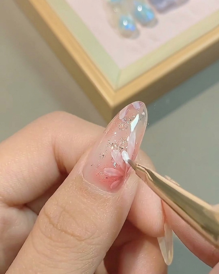 Un pinceau liner fin ajoutant une seconde couche de pétales blancs, superposés sur le design de fleur initial sur un ongle rose.