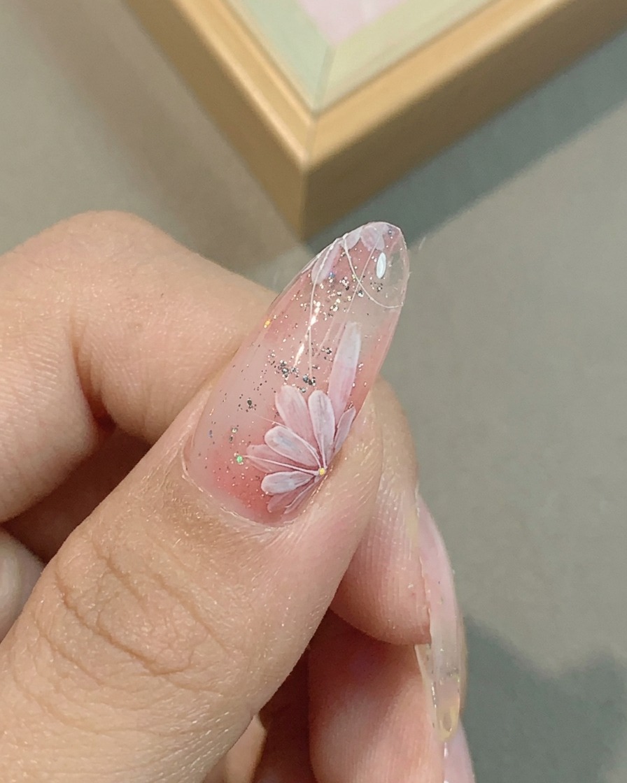 Gros plan dun ongle avec des pétales de marguerite roses en cours daffinage avec un pinceau liner fin.