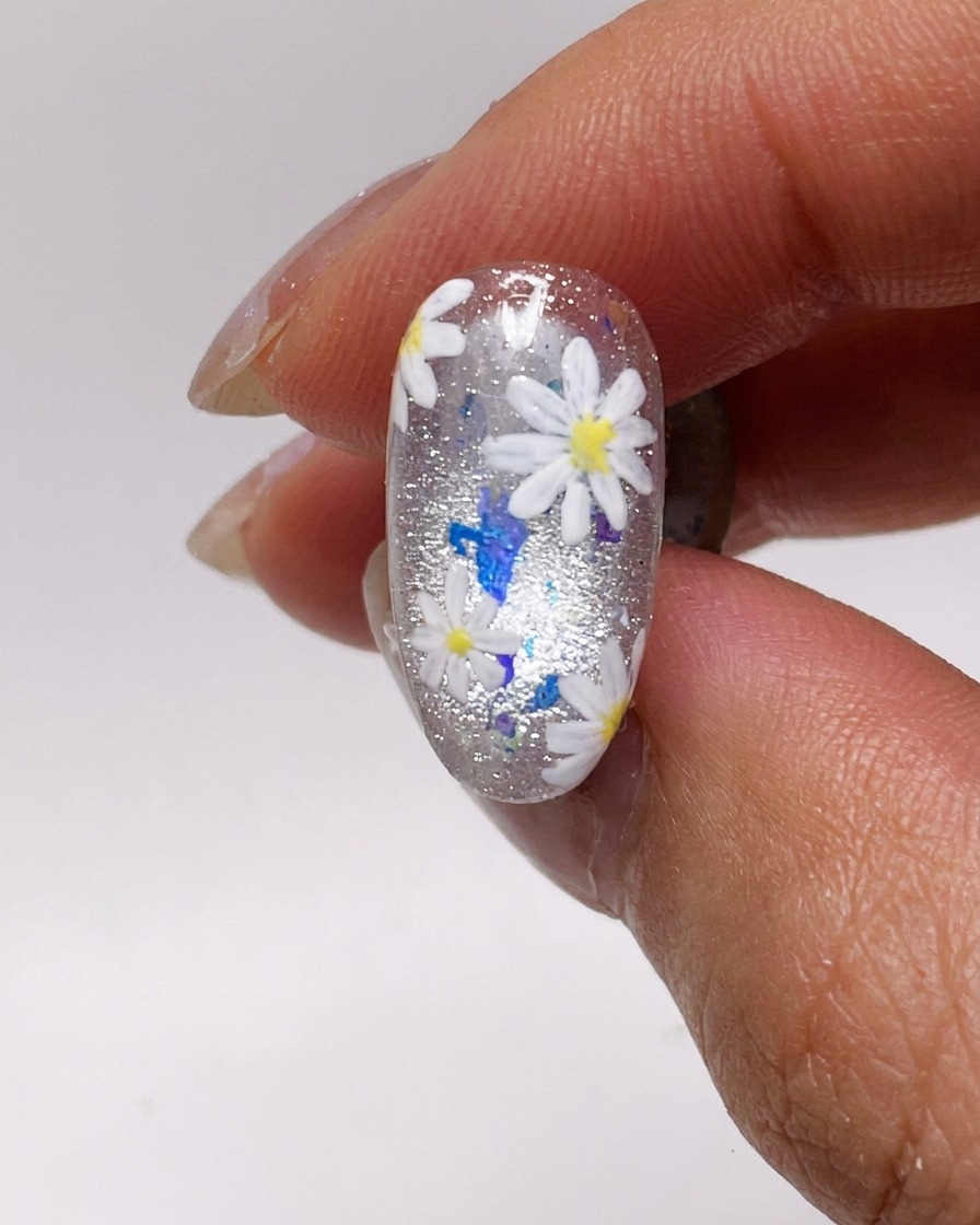 Gros plan sur un pinceau appliquant une fine couche de vernis gel cat-eye argenté sur un ongle naturel.