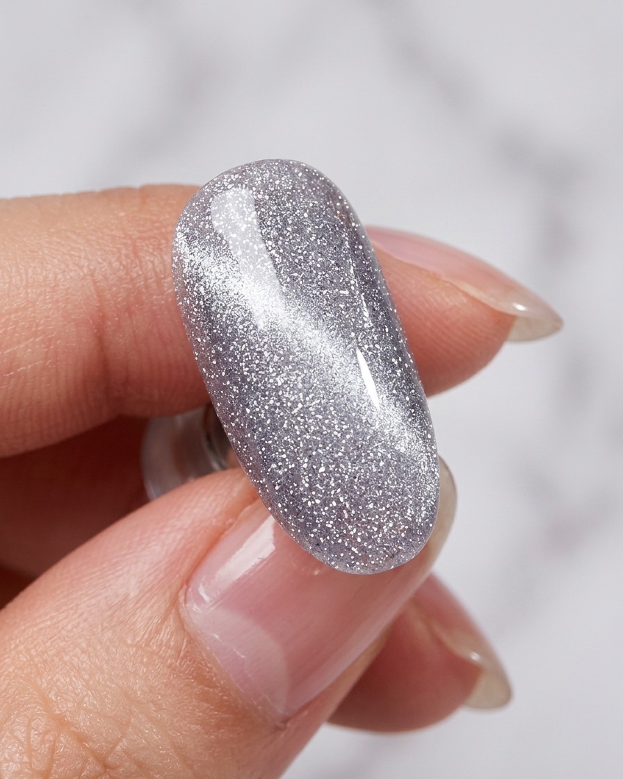 Un outil aimanté placé près dun ongle recouvert de vernis cat-eye humide, révélant une ligne scintillante.