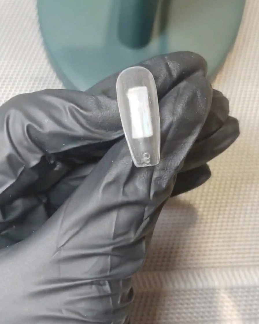 Gros plan sur un ongle avec des points distincts de gel rose nude et blanc laiteux placés au centre de la surface.