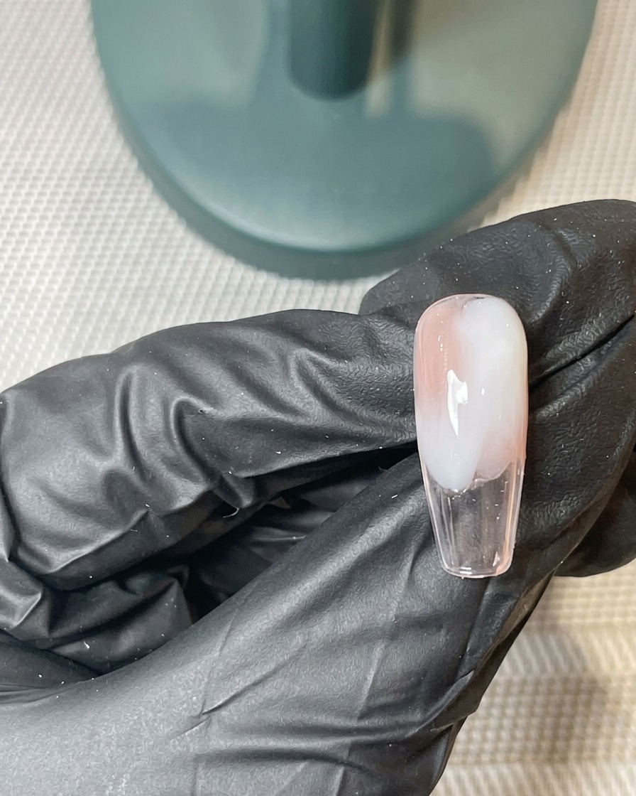 Un pinceau appliquant une deuxième fine couche de gel rose et blanc sur la base ombré catalysée.