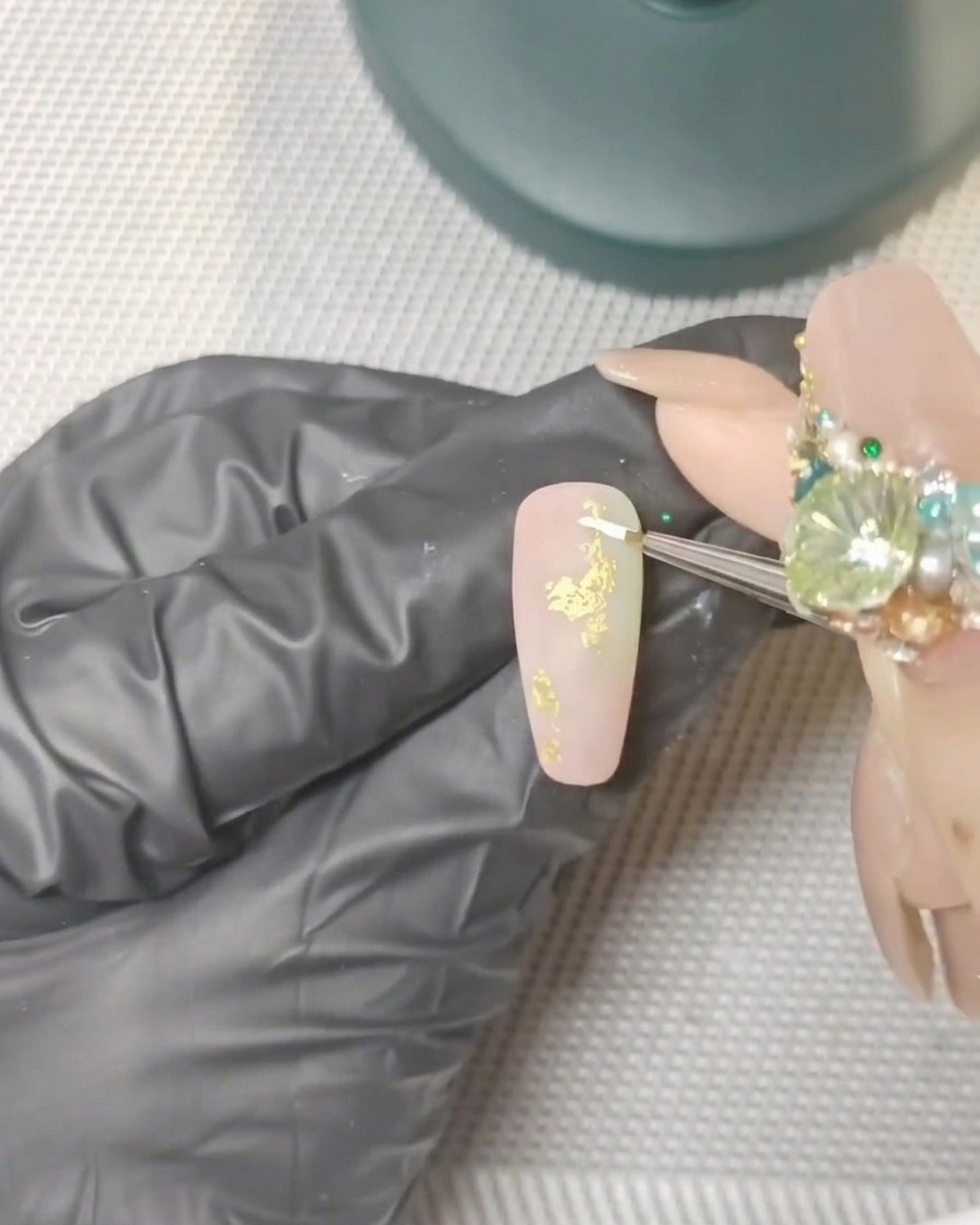 Gros plan sur un pinceau liner fin peignant des formes de pétales blancs sur un ongle fini mat.