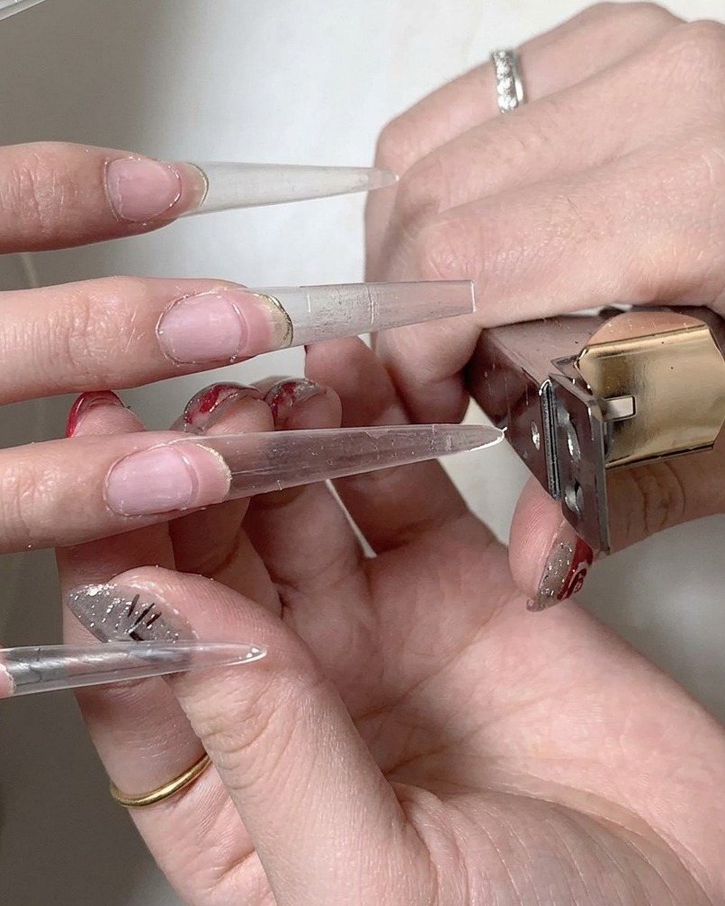 Un pinceau à ongles appliquant une couche de base en gel transparent sur la zone de transition entre longle naturel et lextension.
