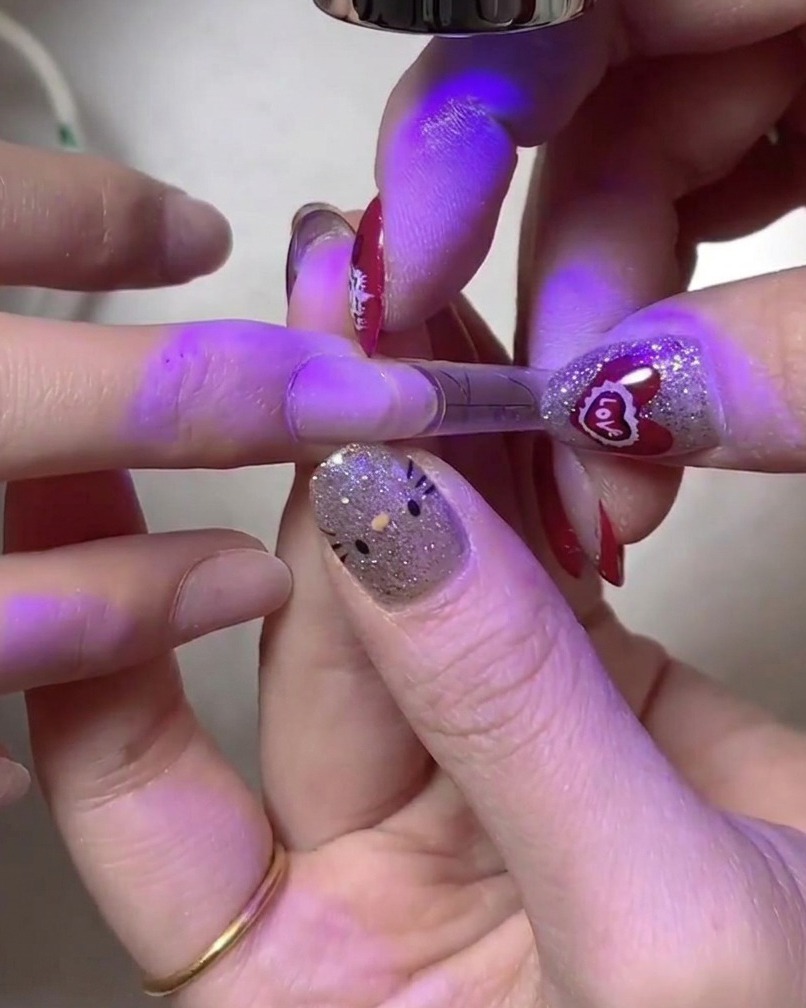 Une main tenant un ongle sous une deuxième lampe UV/LED pour une catalyse approfondie.