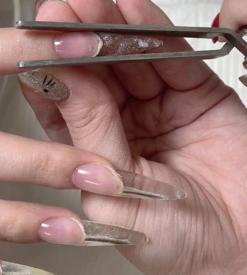 Une pince à épiler métallique soulevant délicatement la forme en plastique de la surface de longle fraîchement catalysé.