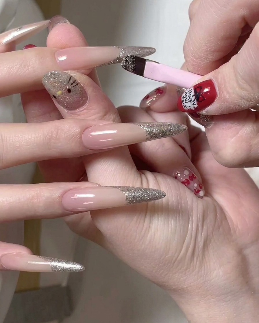 Un pinceau de précision utilisé pour nettoyer le bord dune French manucure à paillettes argentées sur un ongle long.