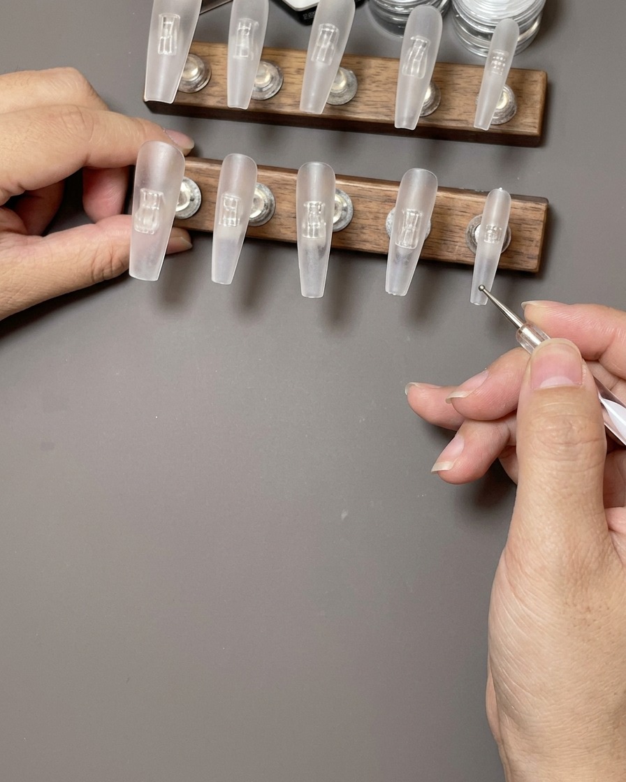 Une main utilisant une lingette non pelucheuse pour nettoyer la surface dun faux ongle transparent.