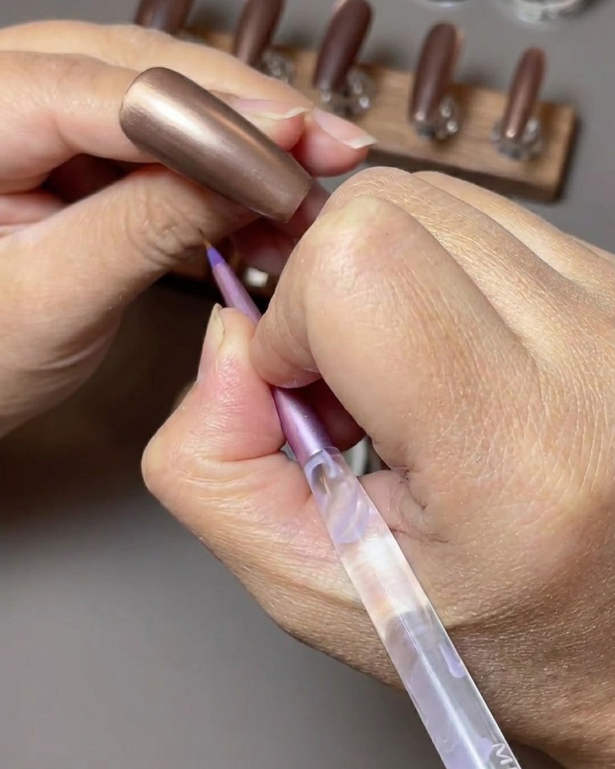 Un pinceau appliquant un vernis gel cat-eye brun toffee riche sur un ongle.