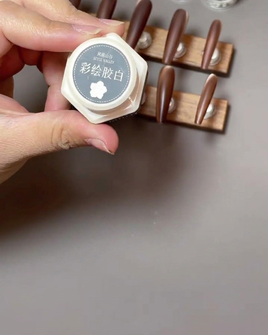 Un pinceau liner fin dessinant des pétales blancs délicats en forme de parenthèses pour un design de rose sur un ongle brun mat.
