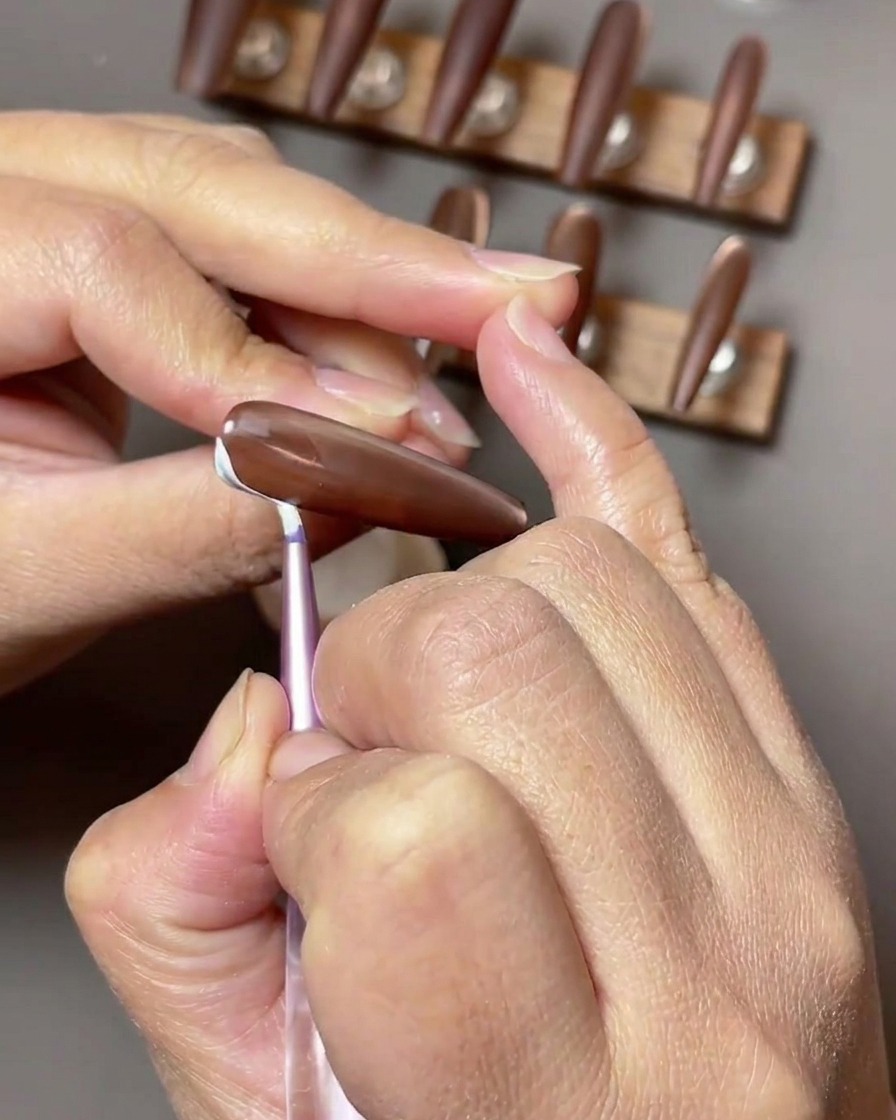 Gros plan sur un ongle brun où des traits délicats en forme de ruban blanc sont peints le long du côté de la surface de longle.