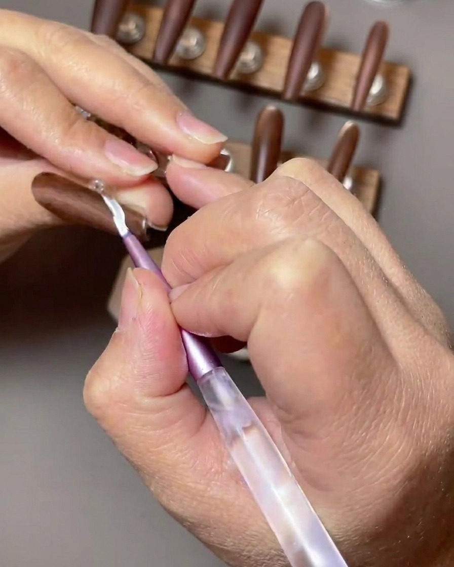 Gros plan sur un ongle brun accentué avec un design de French manucure blanche appliqué avec un pinceau nail art fin.