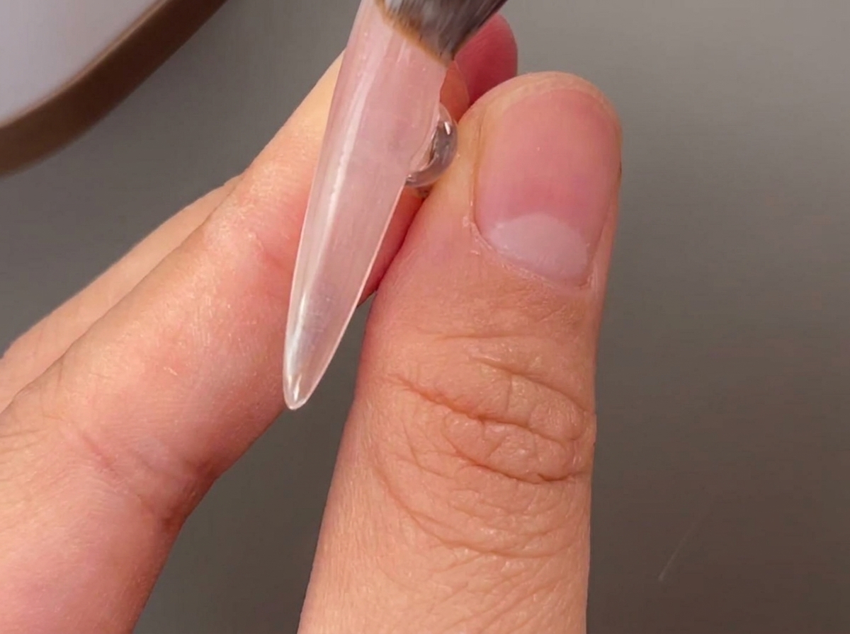 Un pinceau appliquant une couche de gel de base transparent sur un ongle naturel.