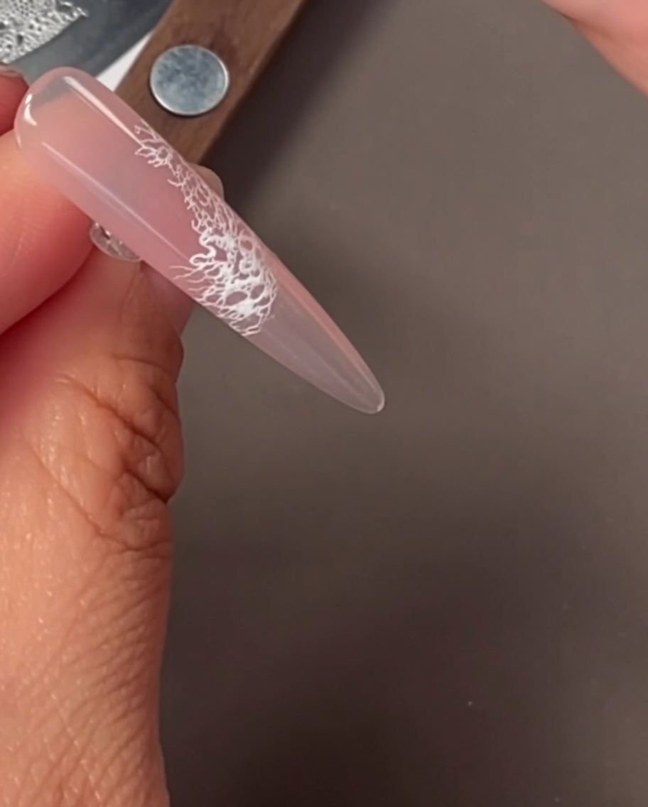 Un gros plan sur un ongle avec un motif de dentelle blanche délicat appliqué par stamping.