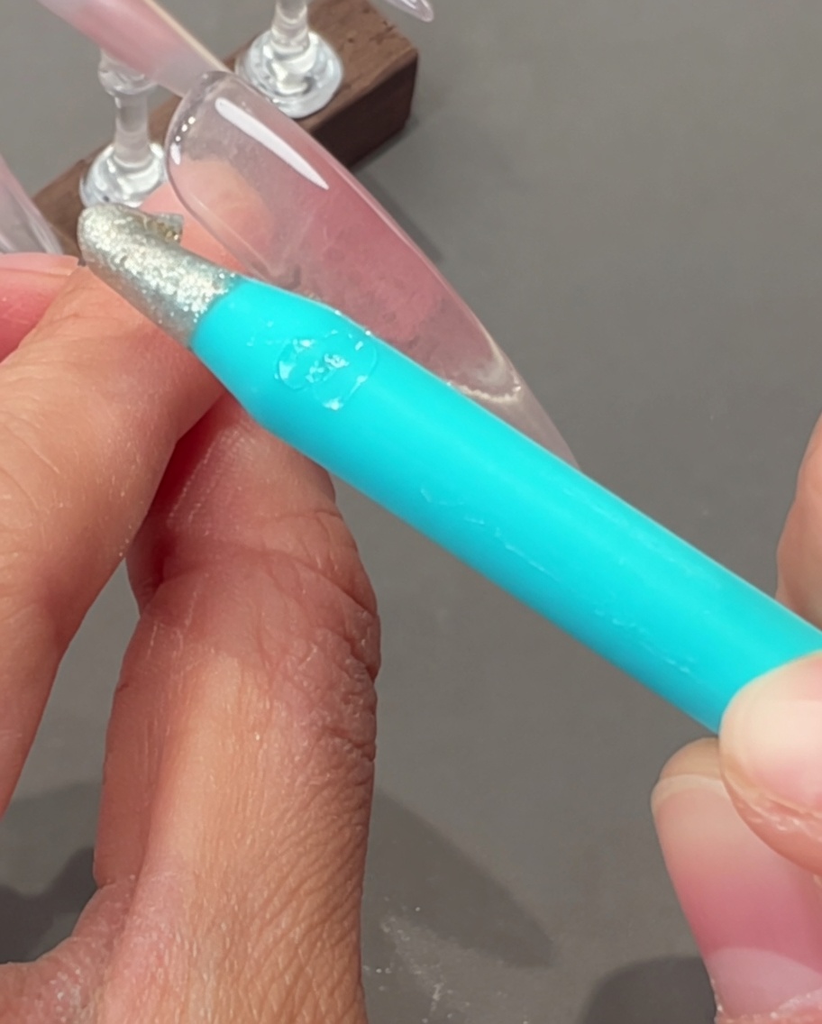 Une main tenant un pinceau liner fin, traçant de fines lignes argentées sur la surface dun ongle.