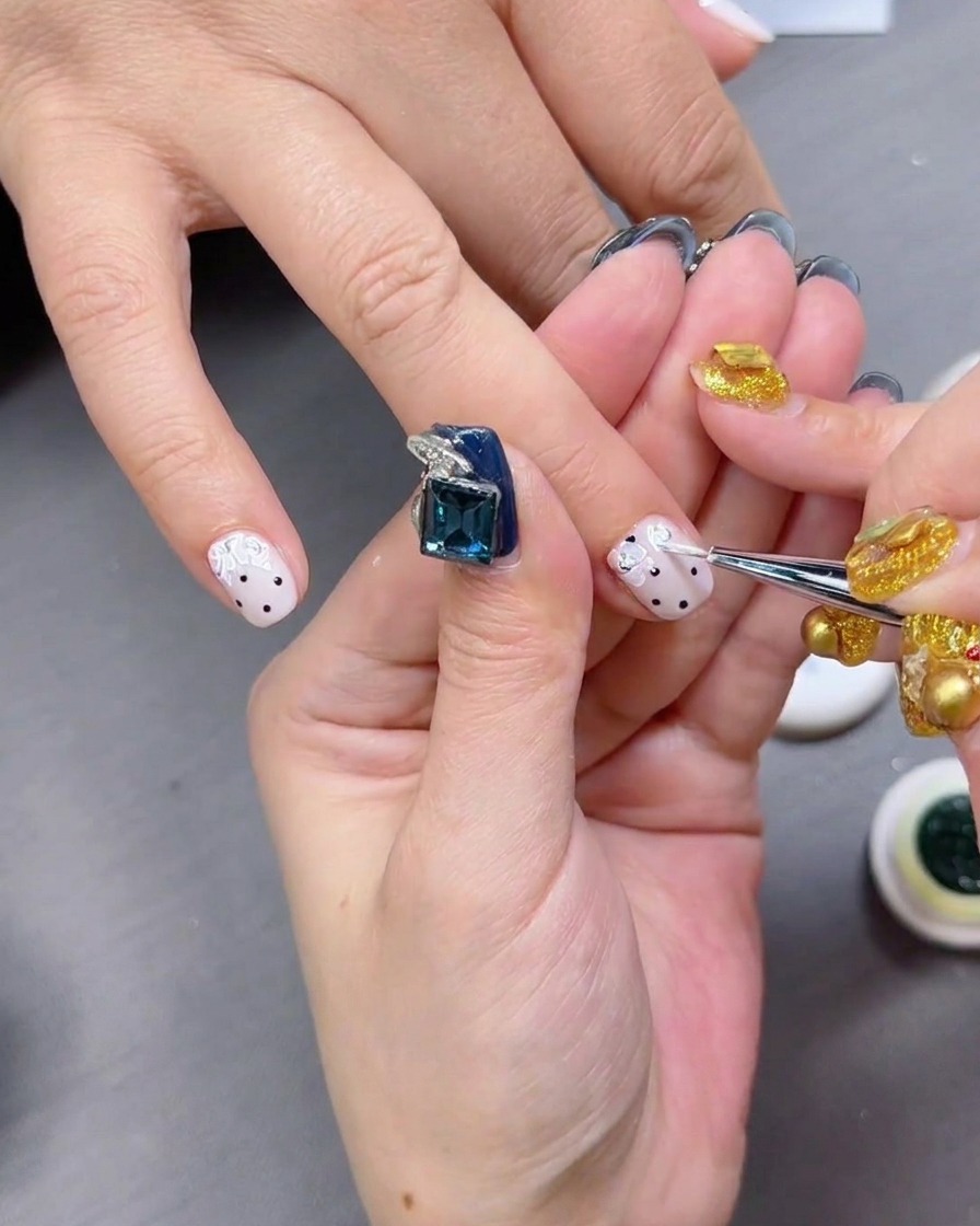 Application dun top coat brillant sur des ongles à pois noirs.