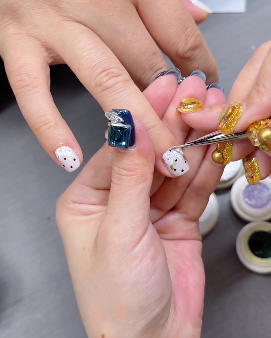 Gros plan sur une main aux ongles décorés de fleurs placée sous une lampe LED professionnelle.