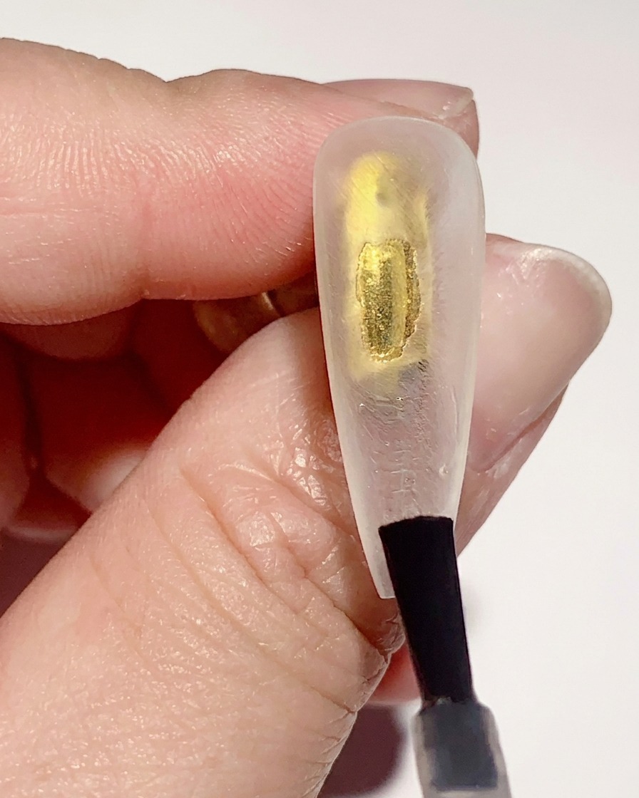 Un pinceau appliquant une fine couche de base coat en gel transparent sur la surface interne dune capsule transparente.