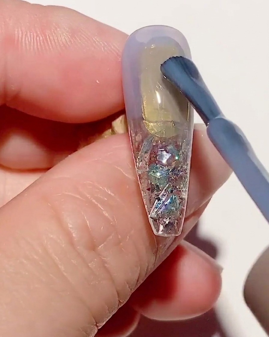 Un pinceau appliquant une fine couche de vernis gel bleu transparent sur une capsule texturée.