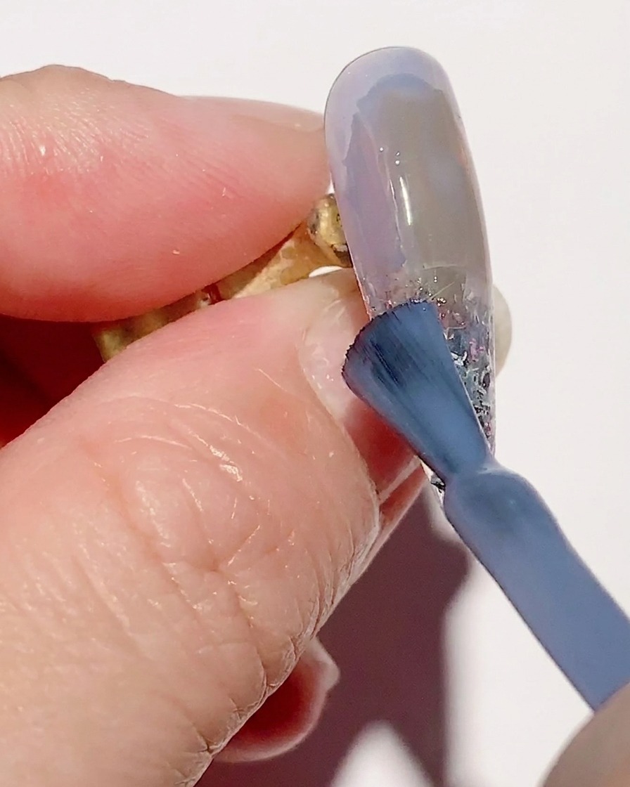 Un pinceau dégradé estompant du vernis gel bleu transparent sur la surface de longle pour une transition fluide.