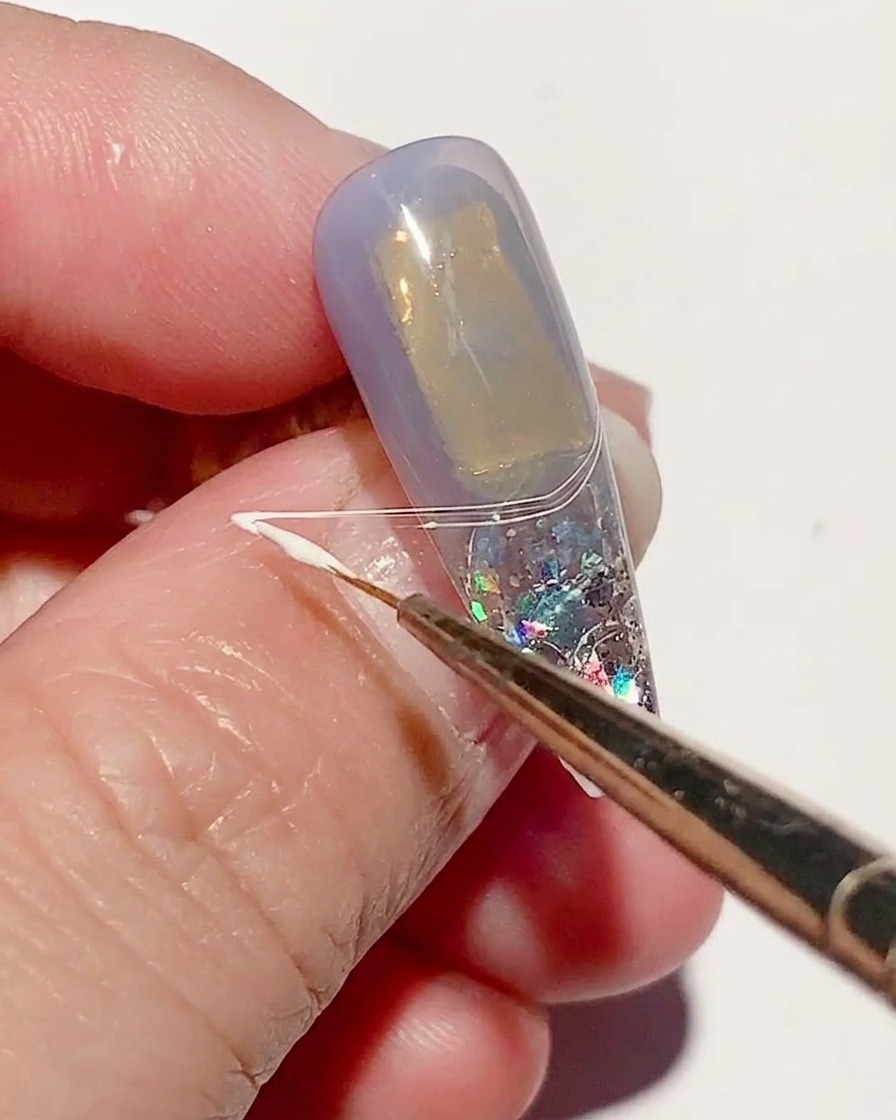 Un pinceau fin étirant du spider gel blanc sur la surface de longle pour créer des lignes fines ressemblant à une toile.