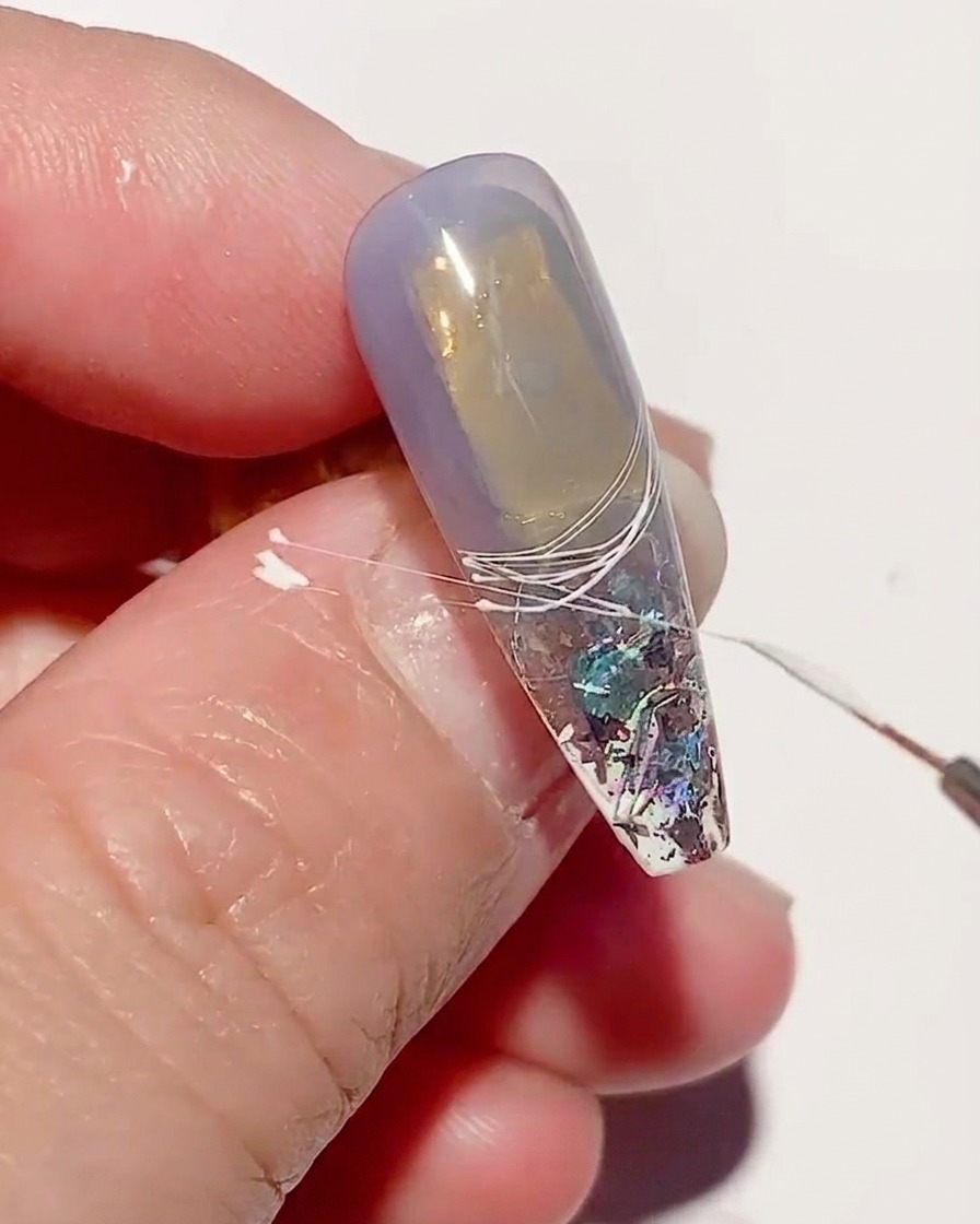 Gros plan sur un ongle avec des lignes de spider gel blanc en cours de catalyse sous une lampe UV.
