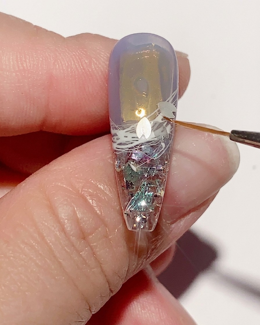 Une pince déposant de petites paillettes délicates en forme de fleur de cerisier sur la surface de gel humide dun ongle.
