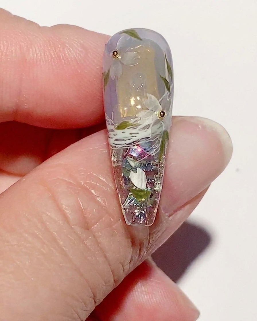 Un ongle manucuré avec un art fleurs de cerisier, montrant un top coat brillant appliqué sur tout le design.