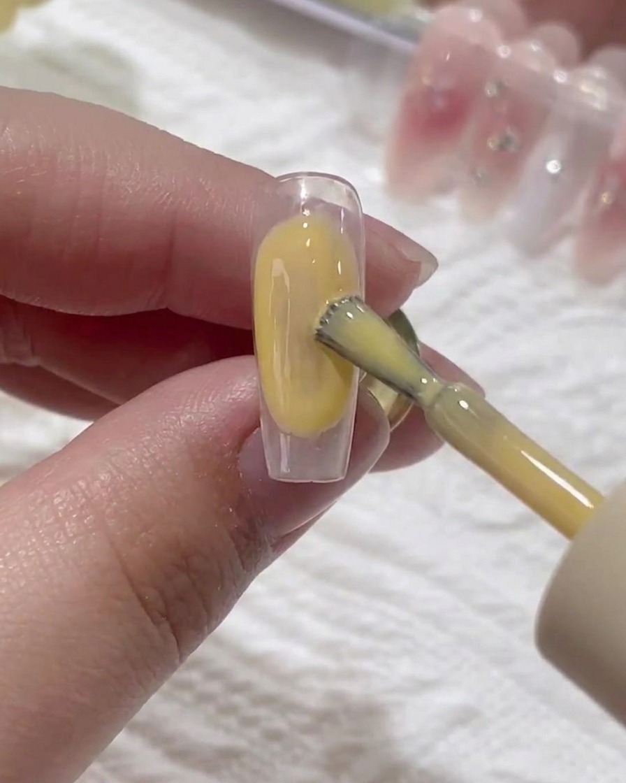 Un pinceau appliquant une fine couche de base transparente sur un ongle naturel.