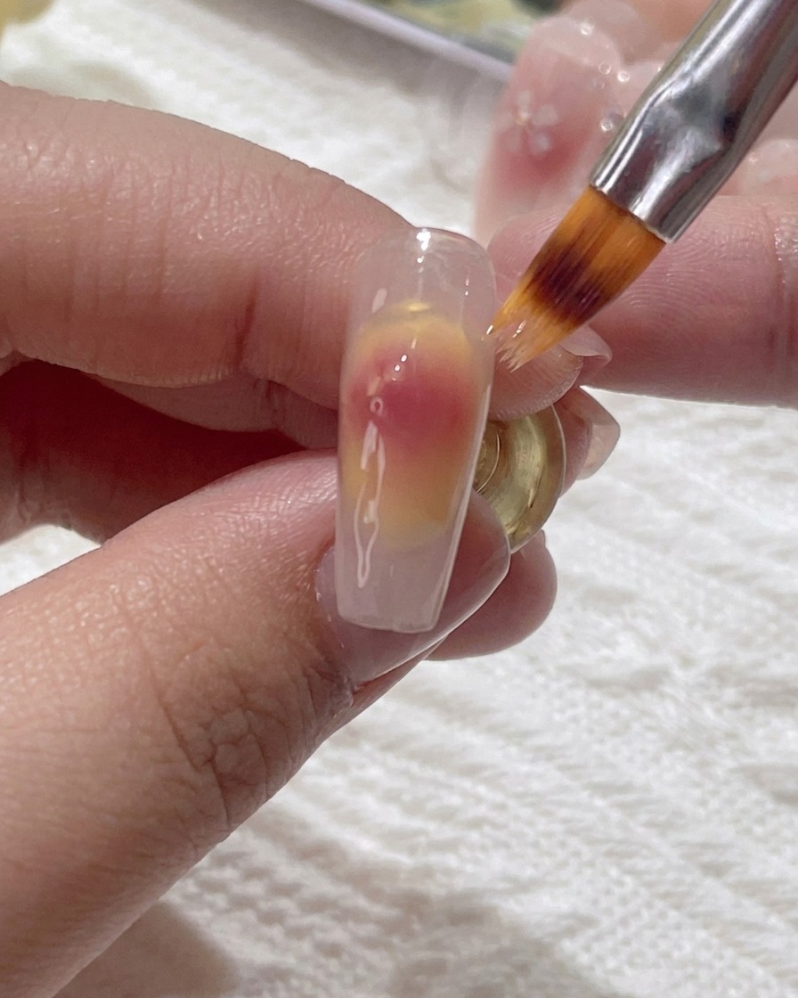 Un pinceau fin estompant délicatement les points de gel rose sur longle.