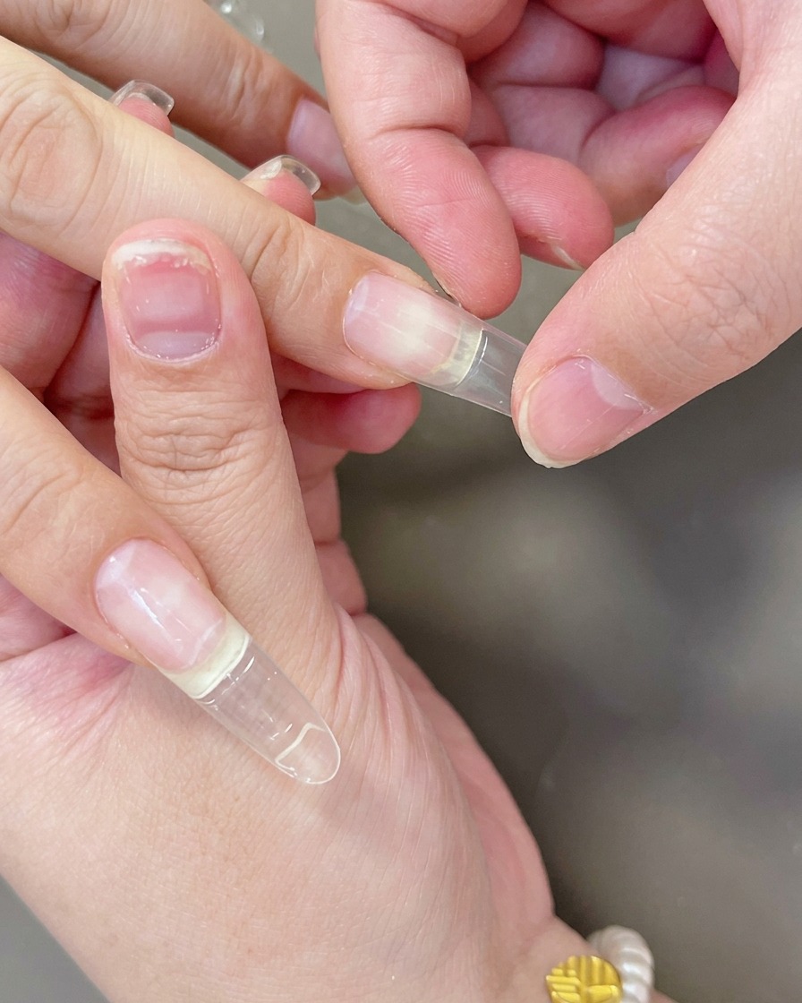 Des doigts pressant une capsule dextension en gel transparente sur longle pour assurer une bonne adhérence.