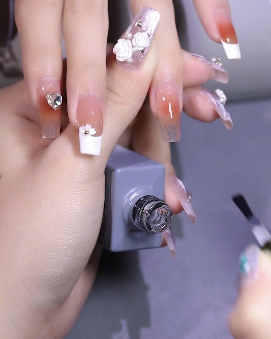 Une pince à épiler plaçant une petite paillette en forme de fleur de cerisier blanche sur la surface dun ongle.