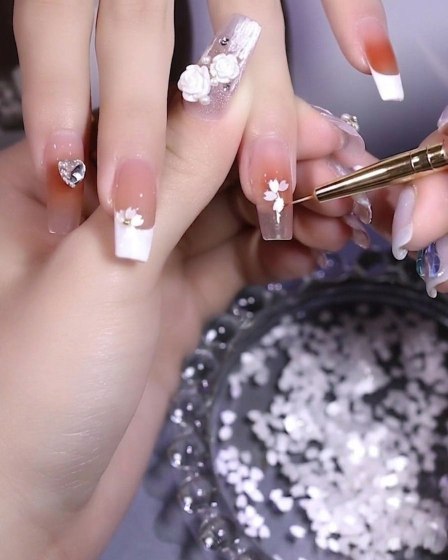 Un gros plan sur un ongle montrant des pétales en train dêtre disposés en forme de fleur avec une pince.