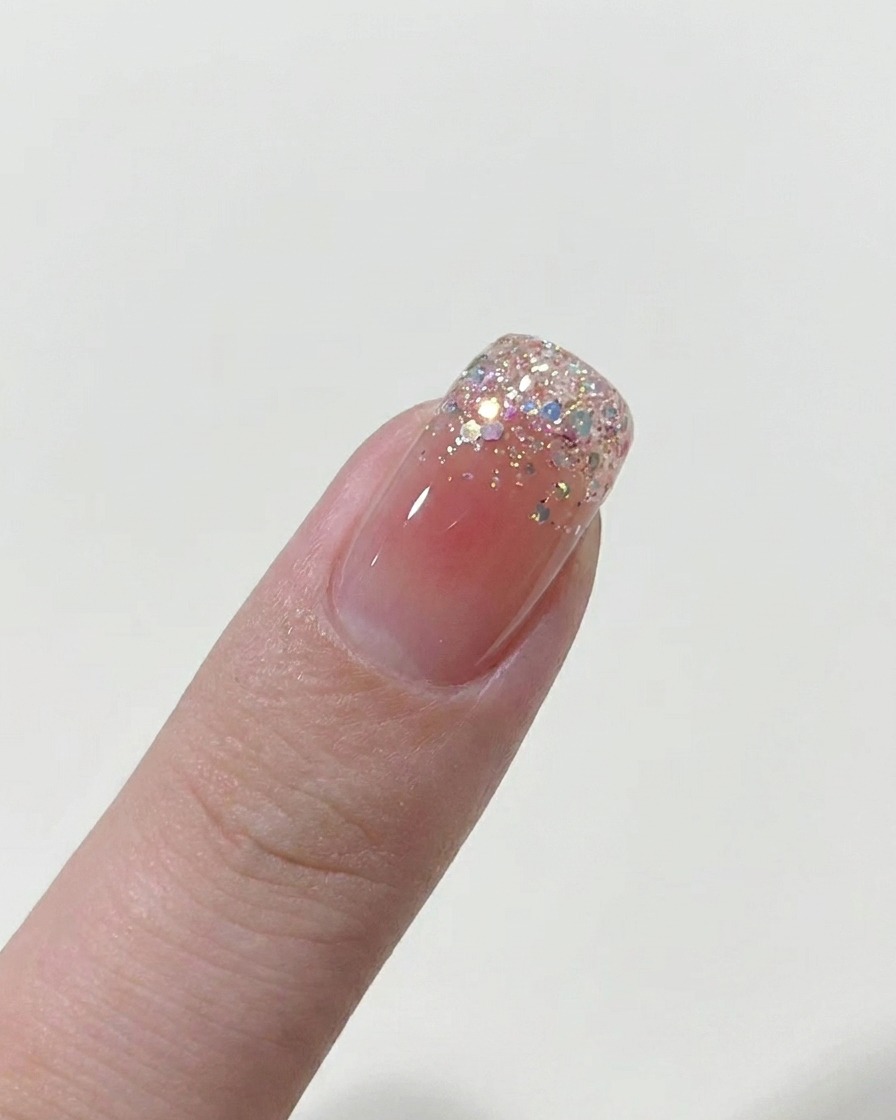 Un pinceau appliquant une fine couche de vernis gel nude sur un ongle nu.