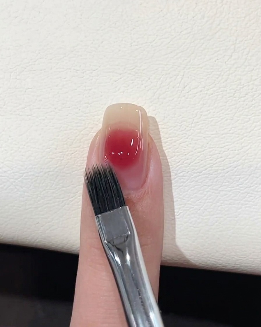 Un pinceau plat destompage adoucissant les bords dun point de gel rose sur un ongle.
