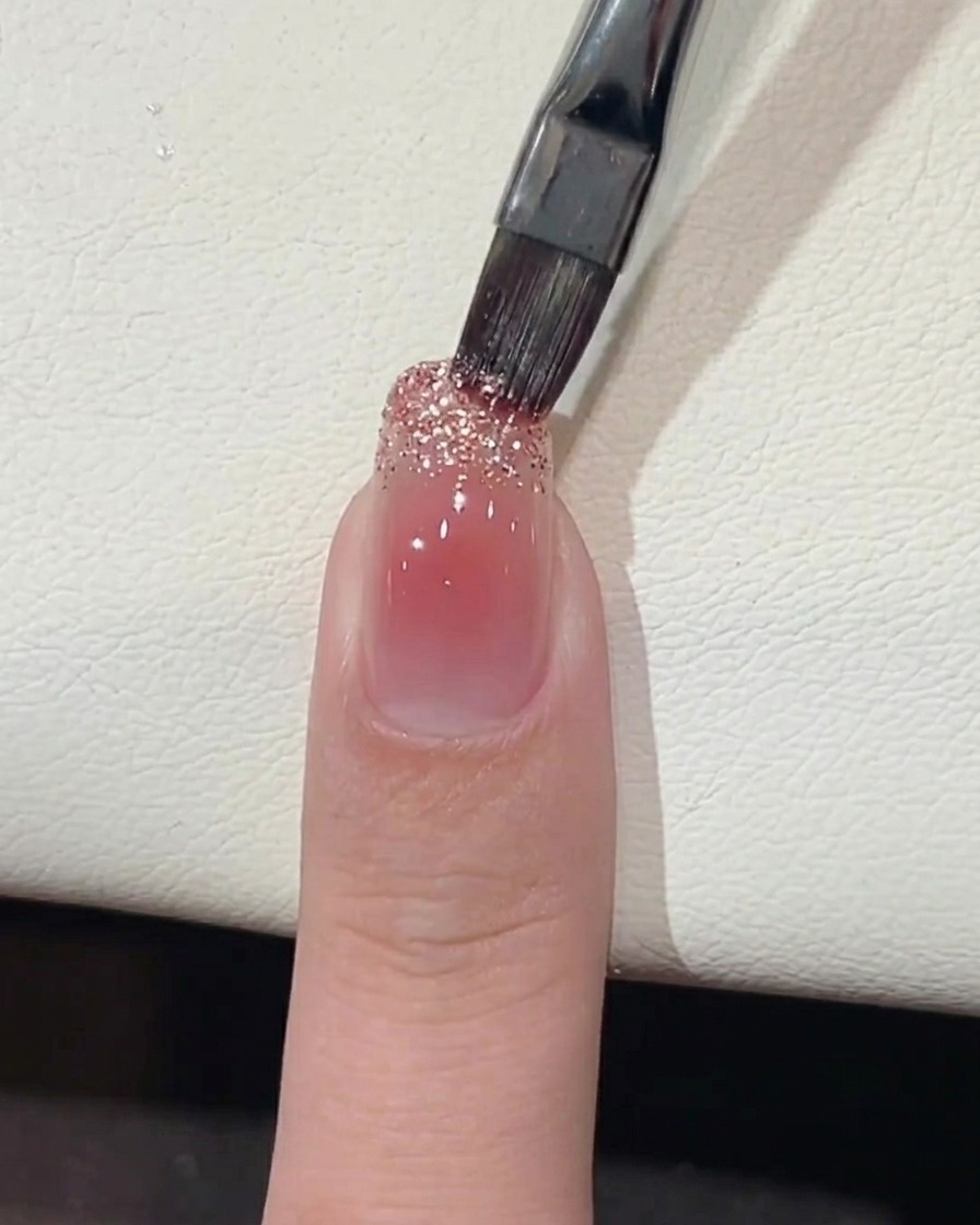 Un pinceau appliquant du gel à grosses paillettes sur le bord libre de longle.