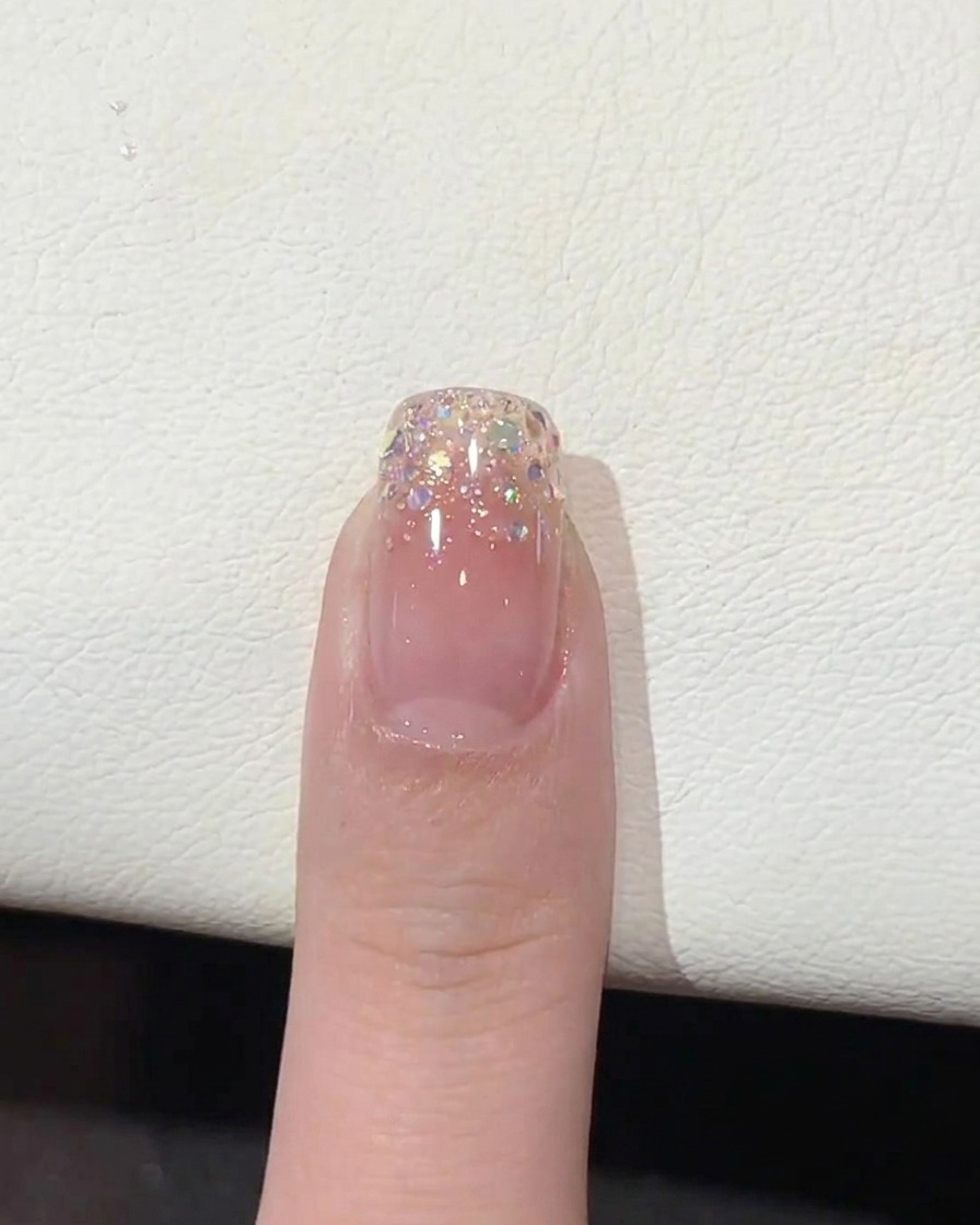 Un pinceau appliquant un top coat brillant et transparent sur le bout de longle en dégradé pailleté.