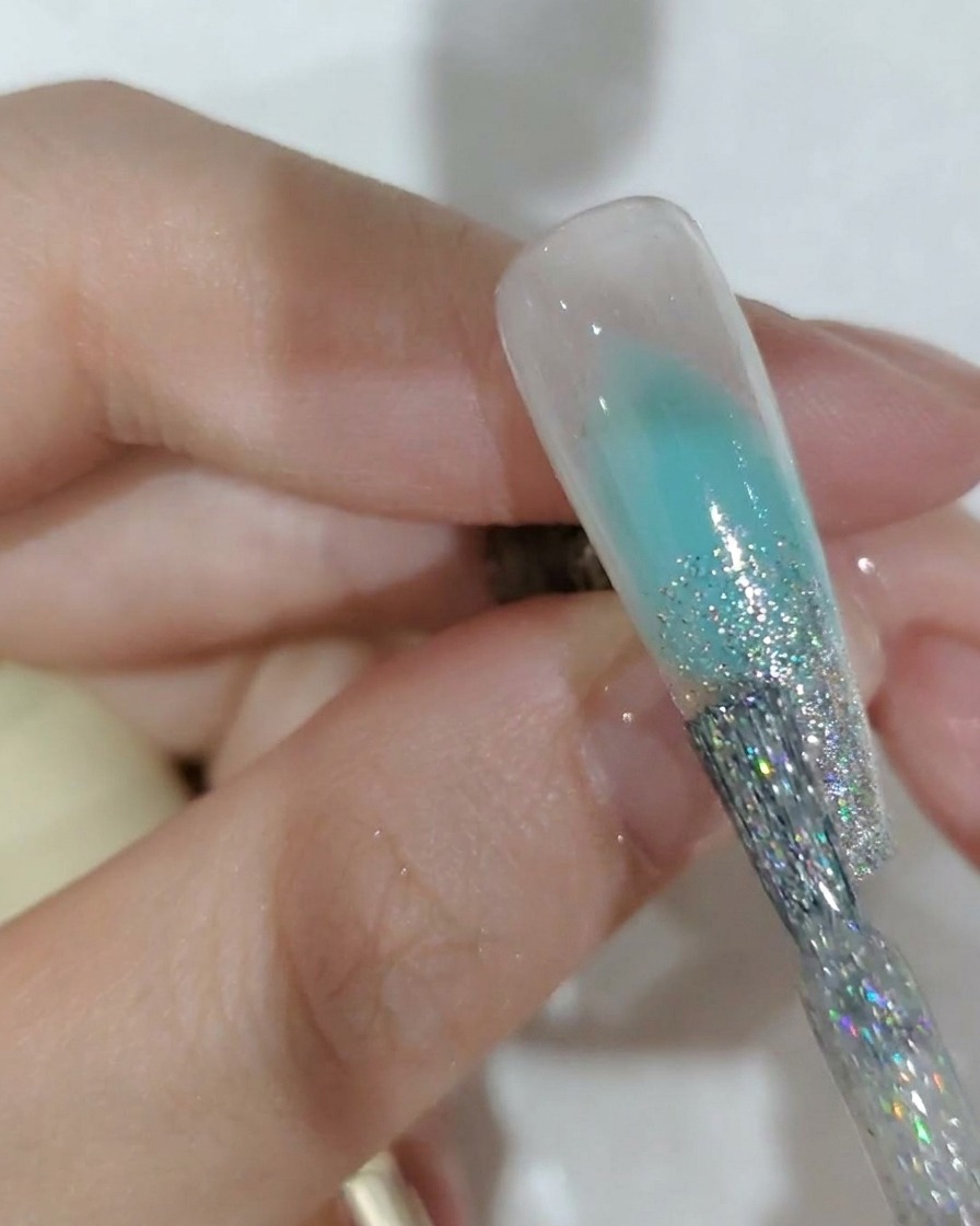 Gros plan dun pinceau appliquant du gel à paillettes argentées sur le bord libre dun ongle.